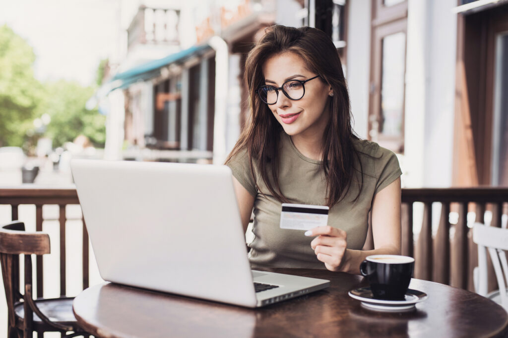 Pareja joven emocionada mostrando tarjeta de crédito y sentado en la mesa de café con computadora portátil acumulando puntos en programas de viajeros frecuentes.