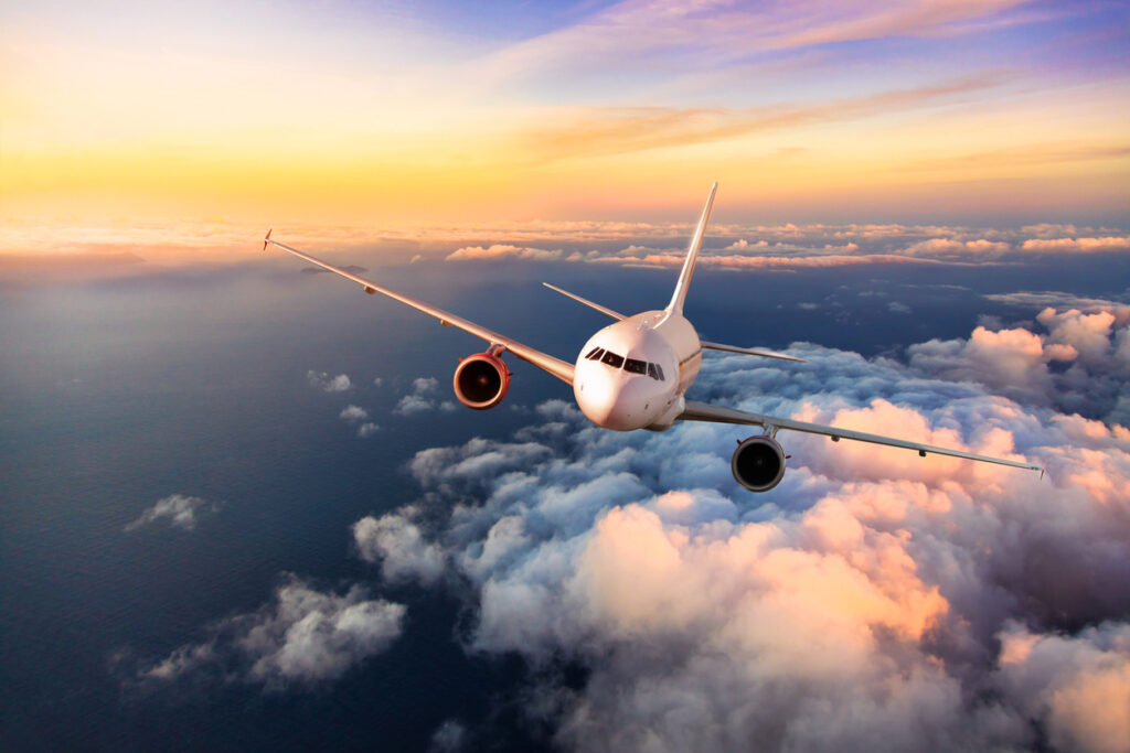 Un avión blanco vuela y está a una altura que permite ver las nubes y el cielo al atardecer
